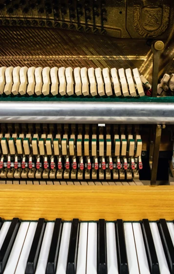A close-up view of an upright piano’s inner mechanics, showing hammers, strings, and the keyboard. A close-up view of an upright piano’s inner mechanics, showing hammers, strings, and the keyboard.